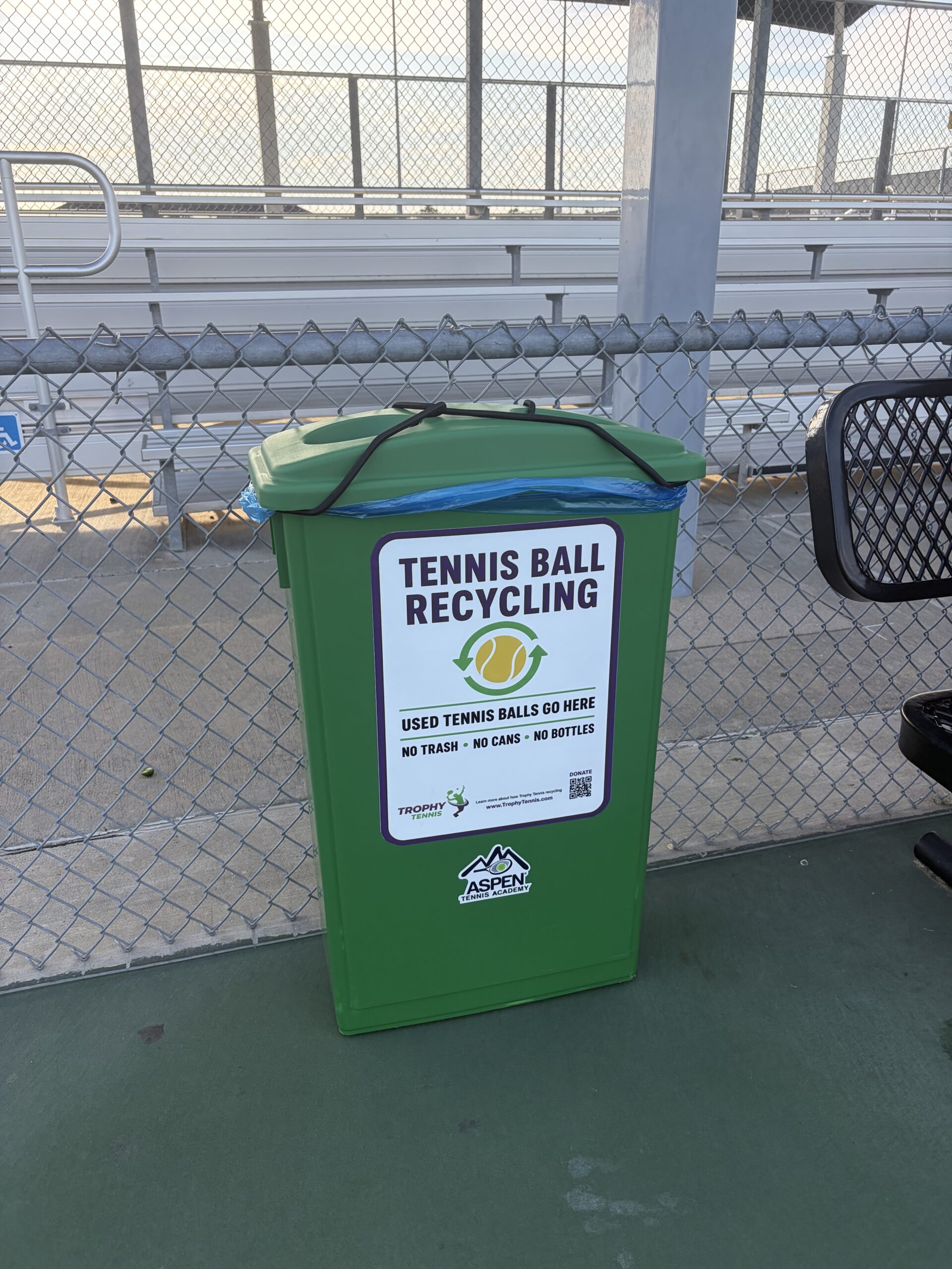 Green tennis ball recycling bin beside a tennis court